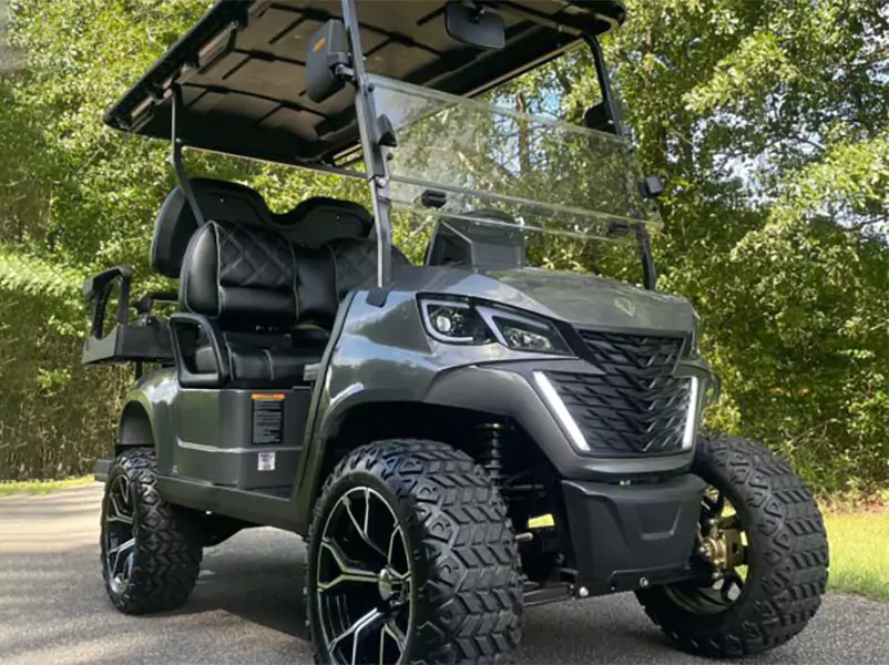 Lifted grey 4-seat golf cart featuring black luxury seats, aggressive off-road tires, full LED lighting, and a tinted windshield parked near trees.