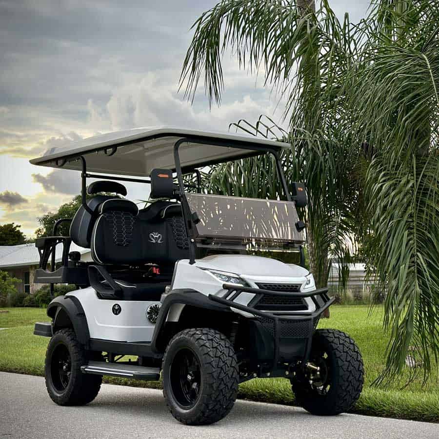 White Venom Electric Vehicles lifted golf cart with black premium diamond-stitched seats and off-road tires parked near palm trees, showcasing a stylish street-legal Venom EV multi-passenger cart.