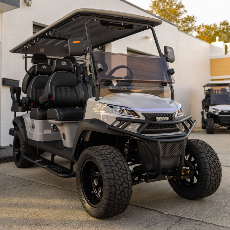 Silver Venom Electric Vehicles lifted golf cart with off-road tires and premium black diamond-stitched seats parked outside a dealership, showcasing a luxury street-legal Venom EV multi-passenger cart.