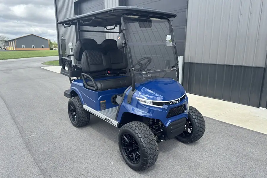 A blue lifted golf cart with off-road tires, front-facing seats, and a windshield parked outside a dealership, showcasing a custom golf cart upgrade ideal for family and recreational use in Indianapolis.