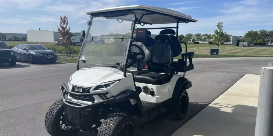 White lifted Voyager electric golf cart with premium black seating and off-road tires parked outside Hurricane Golf Carts in Indianapolis.