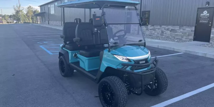 Turquoise 4-seat Voyager golf cart with tinted windshield, rugged off-road wheels, and premium seating in front of Hurricane Golf Carts showroom
