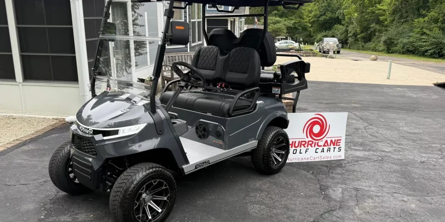 Gray Voyager golf cart parked outside a home with a Hurricane Golf Carts sign in front, showcasing the cart’s lifted wheels and rear seating.