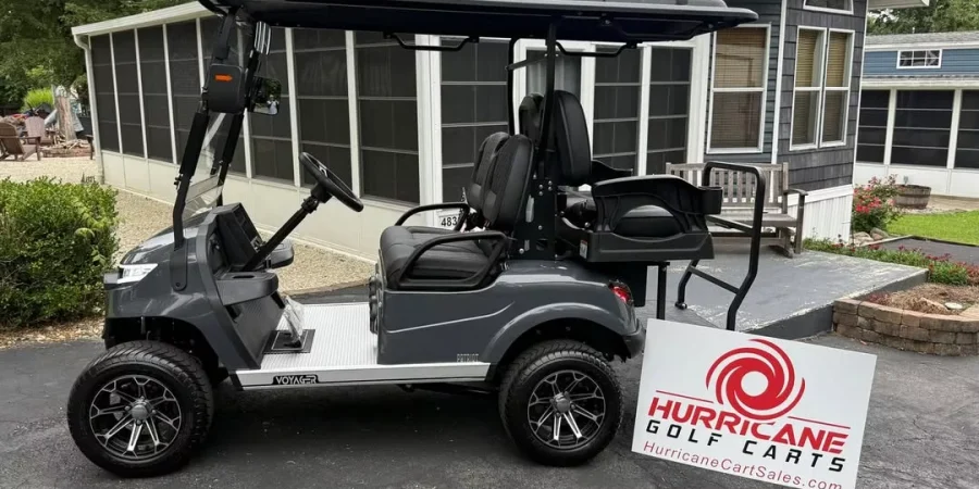 Gray Voyager golf cart parked outside a home with a Hurricane Golf Carts sign in front, showcasing the cart’s lifted wheels and rear seating.