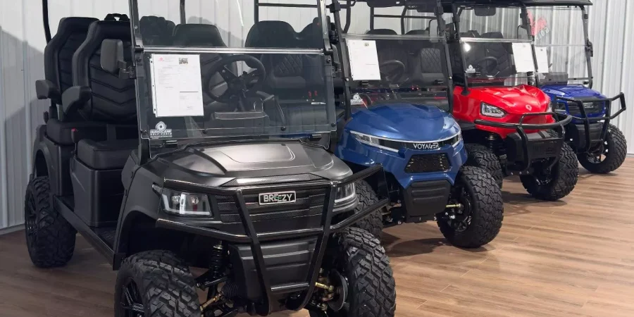 Lineup of Breezy and Voyager golf carts displayed in a showroom, including matte black, blue, and red lifted models with rugged tires and modern seating.